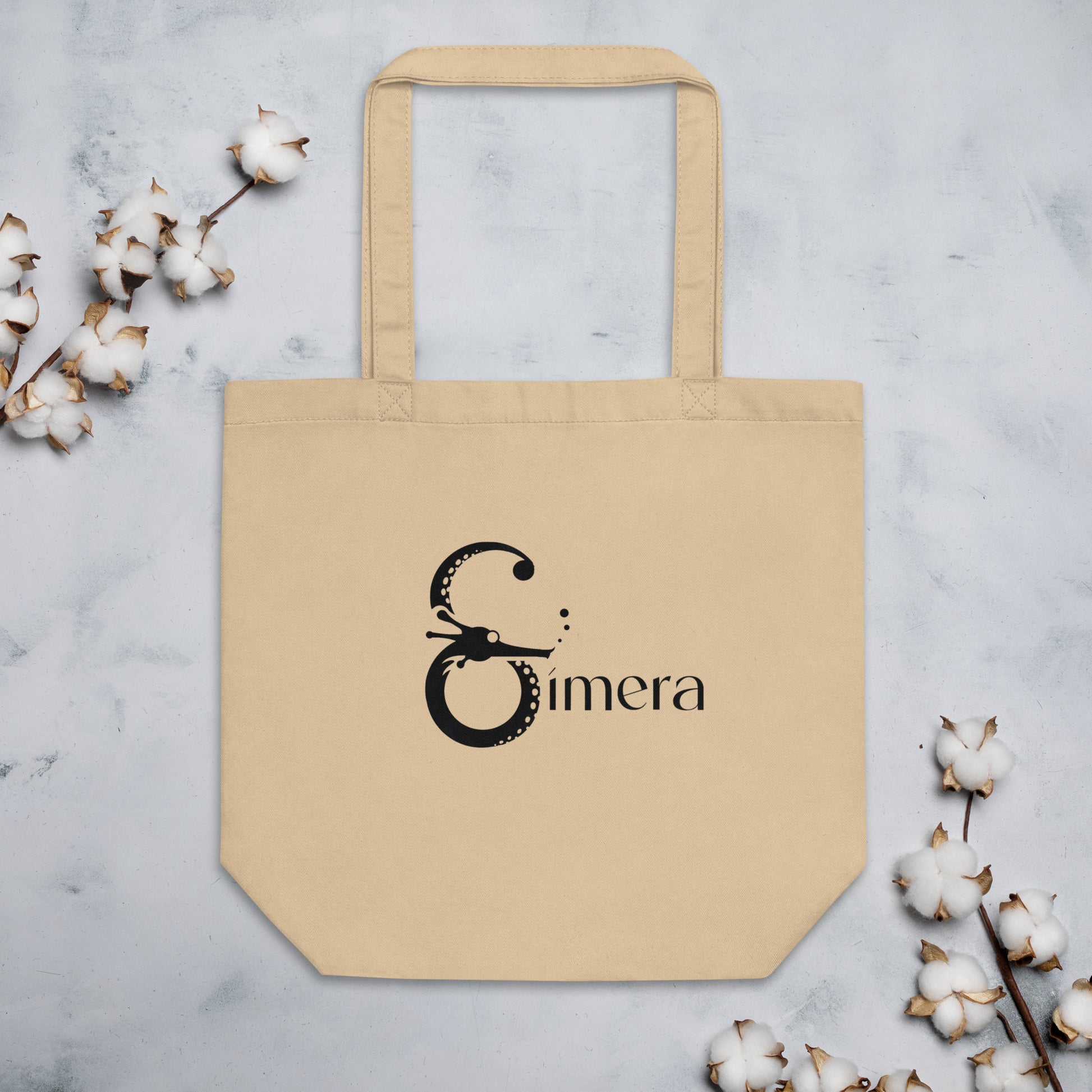 Ecobolsa tote beige colocada en una superficie decorada con ramas y bolas de algodón 100% orgánico, reflejando su uso ecológico y elegante