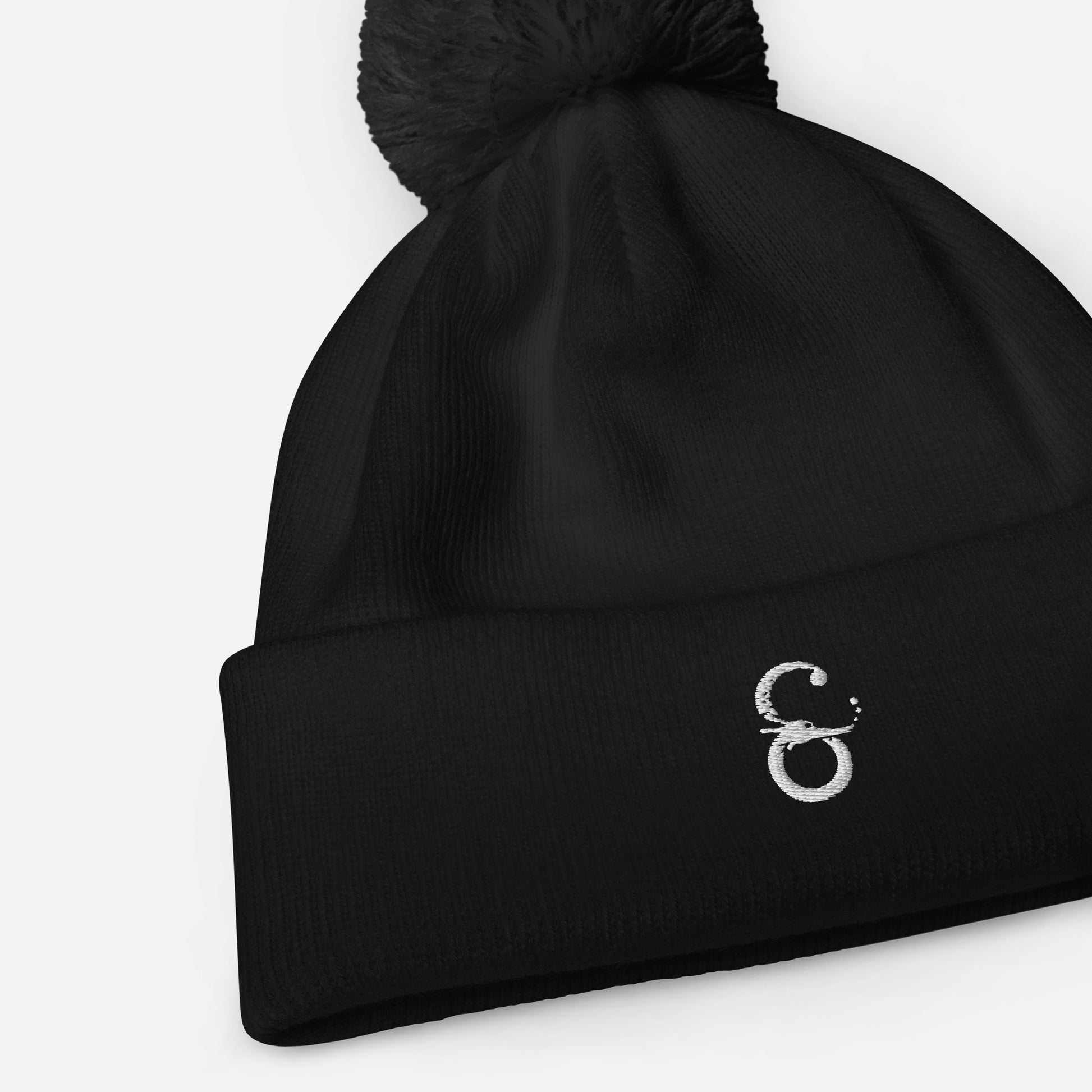 Detalle del tejido acanalado y el logo de Símera-Art bordado en un gorro negro con pompón a juego.